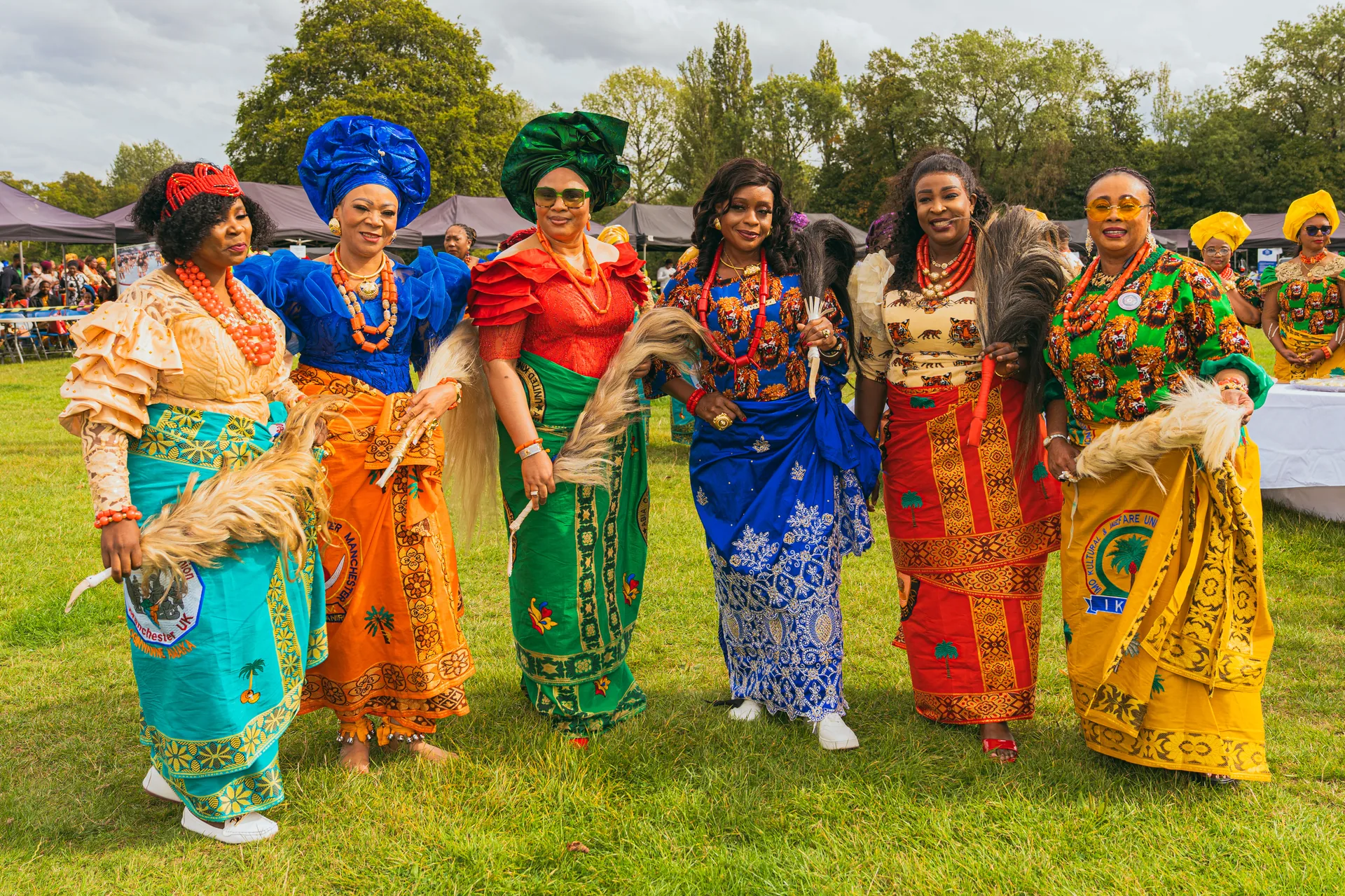 Six women in colourful wrappers holding horsetail fans